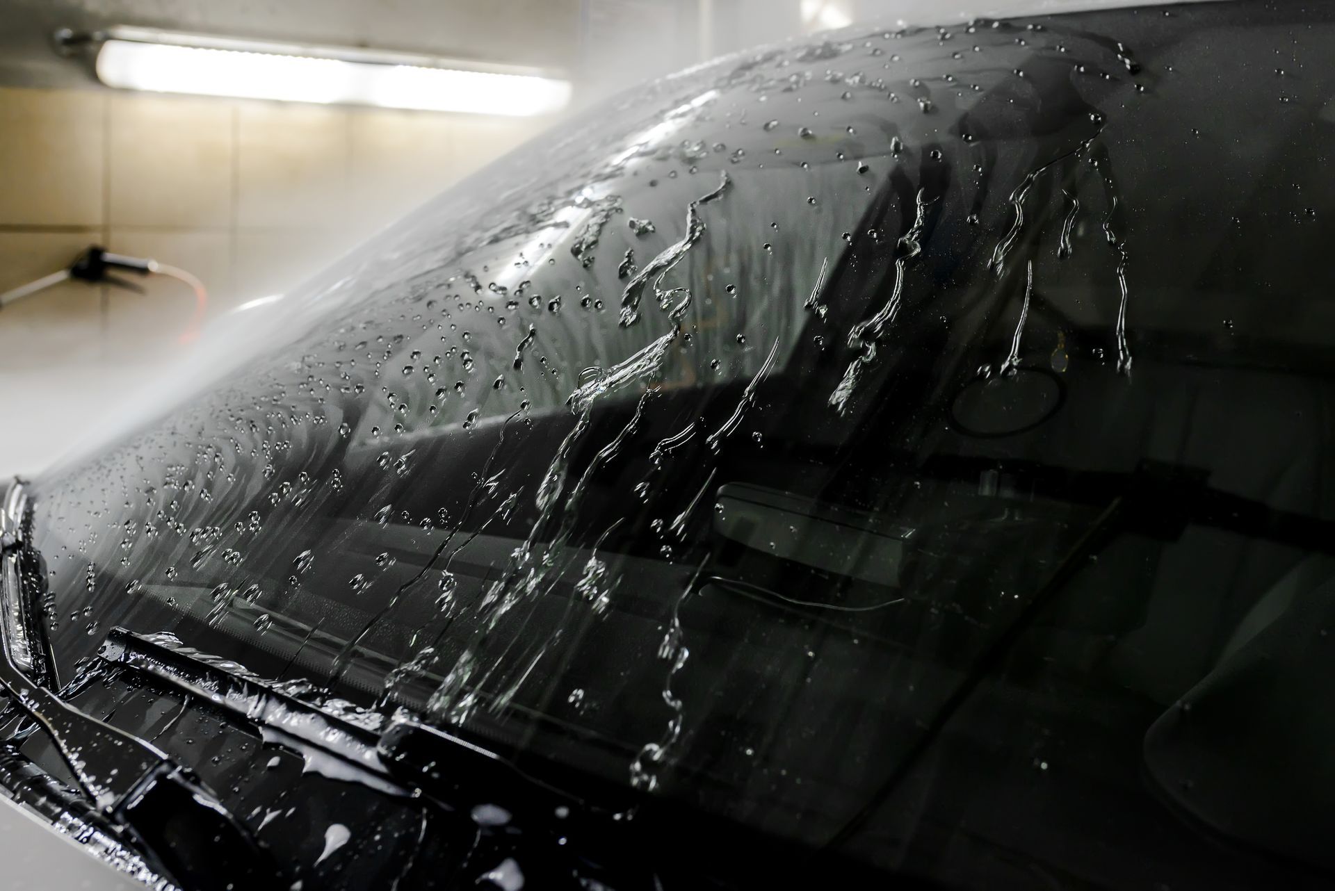 Rain-covered car windshield in a dim garage, with water droplets and wiper marks visible
