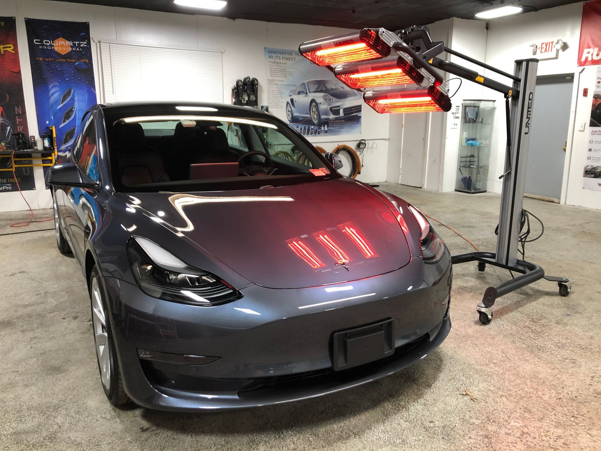 Gray Tesla sedan under red heat lamps in a garage detailing bay