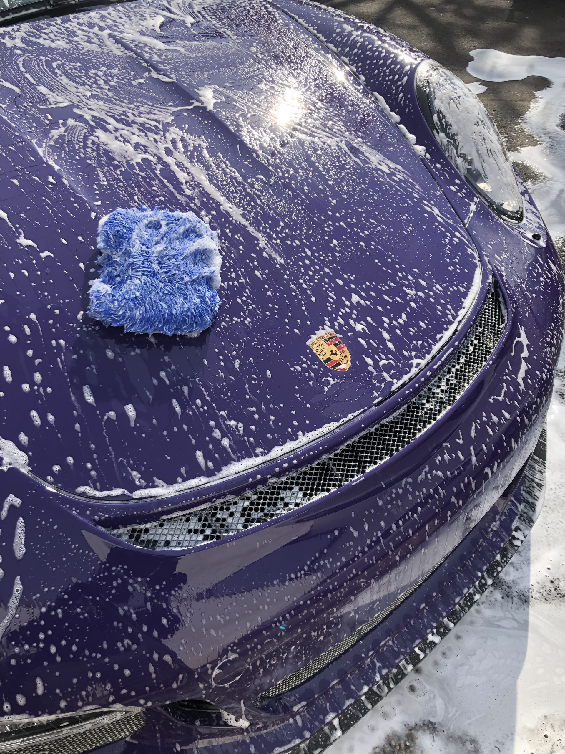 Gloved hand sprays cleaner from a bottle onto a black car door in snowy conditions