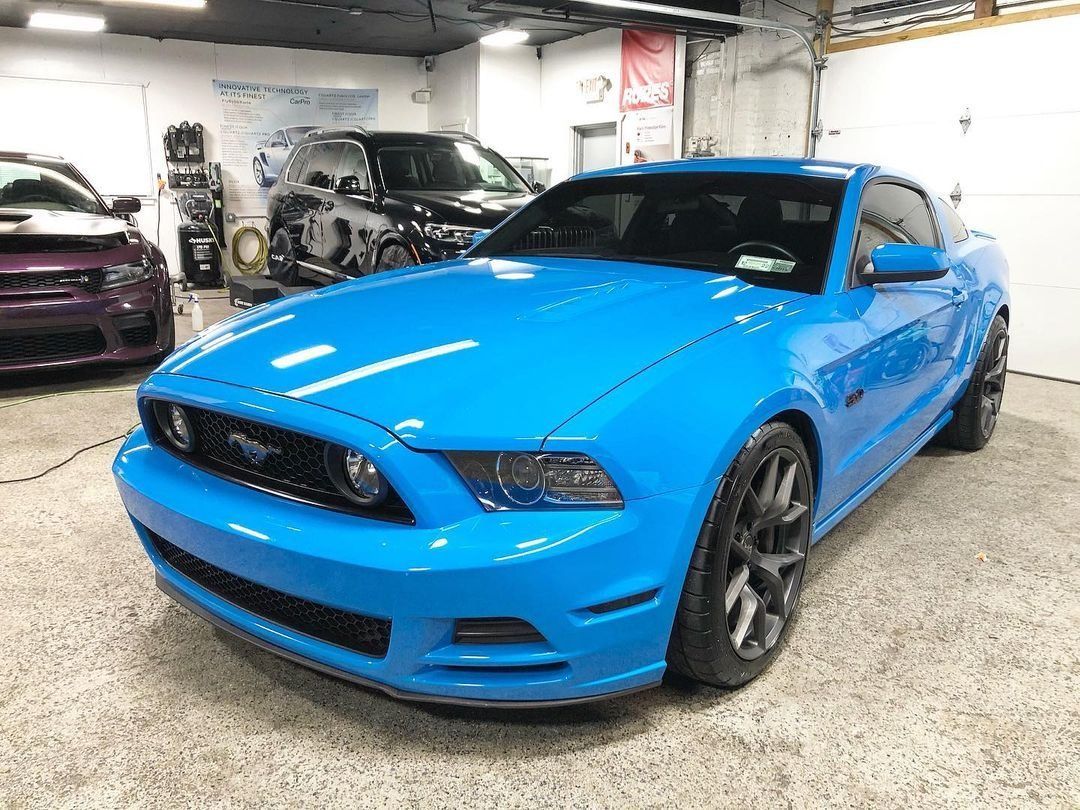 Bright blue Ford Mustang in a garage with other cars in the background