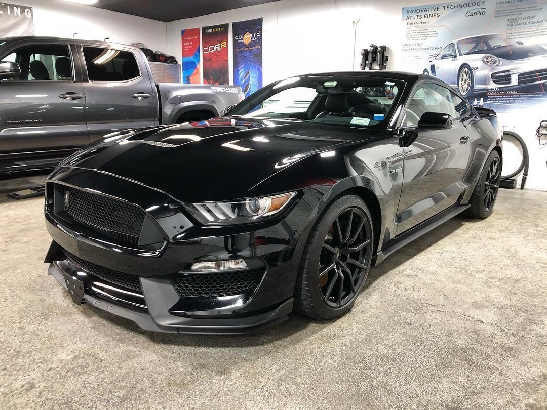 Black sports car in a showroom, angled front view, with glossy paint and custom wheels