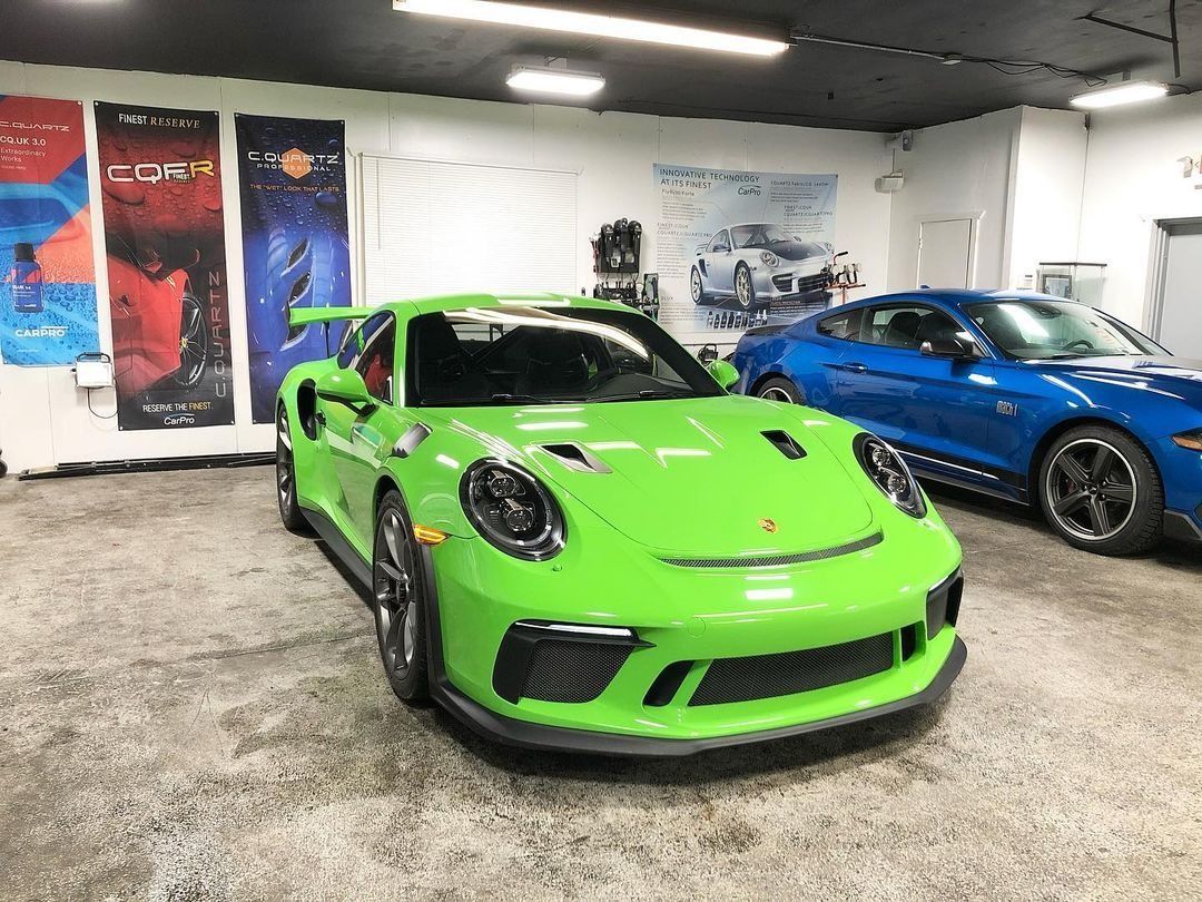 Bright green Porsche parked indoors beside a blue car in a showroom garage