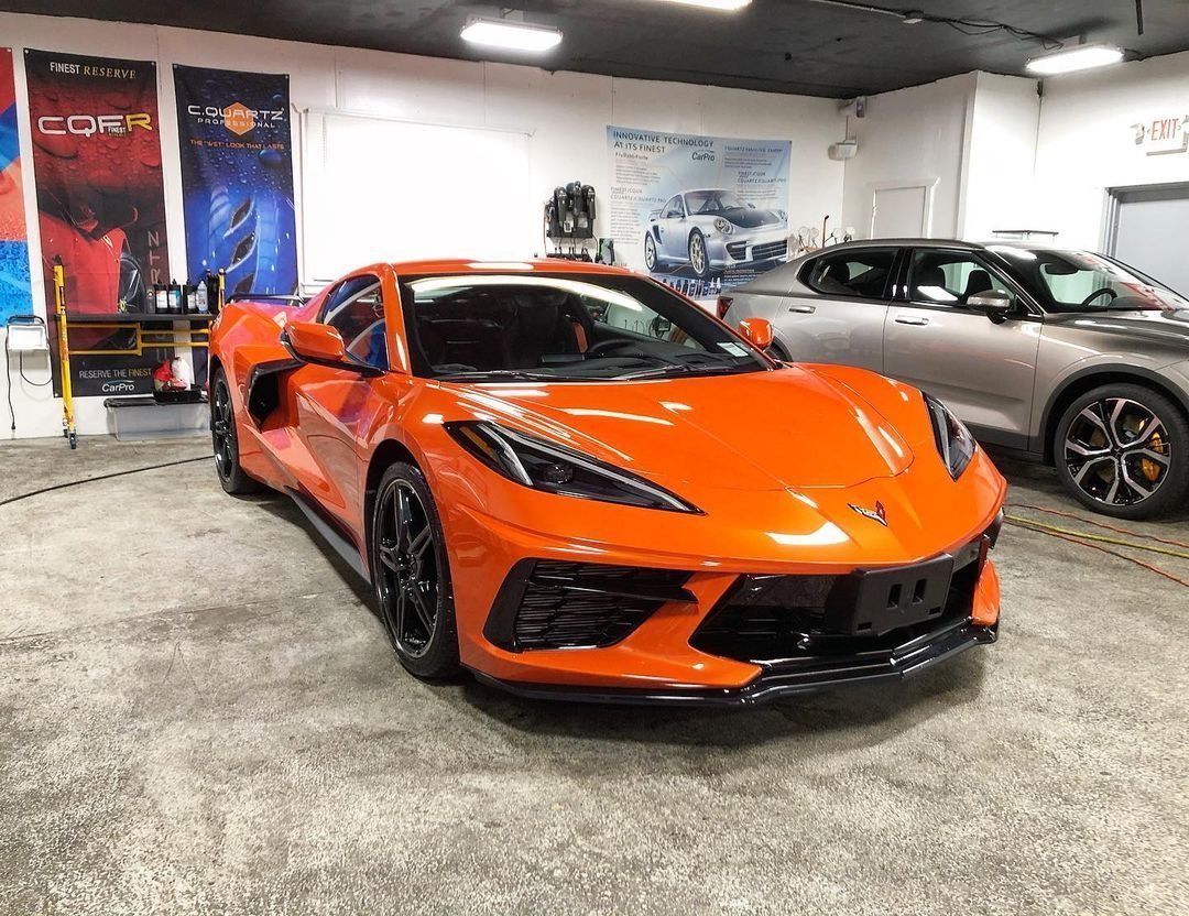 Orange sports car in a showroom, with a silver car parked behind it.
