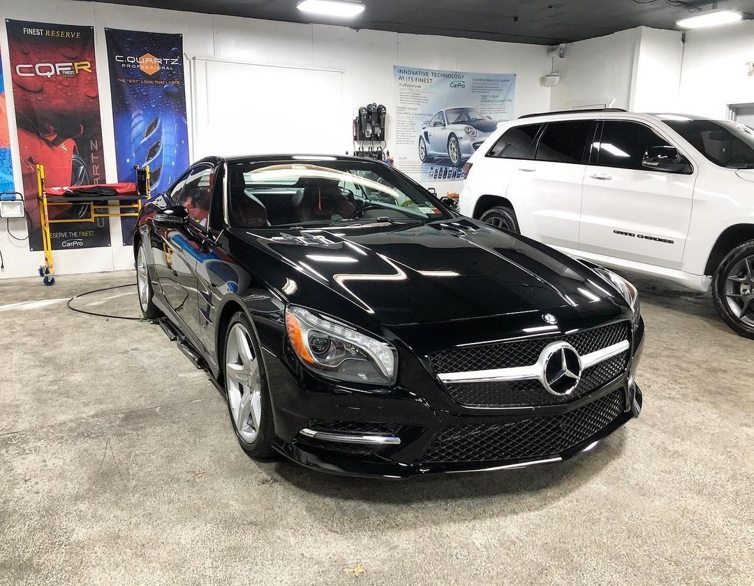 Black Mercedes-Benz coupe in a showroom, with a white SUV parked beside it.