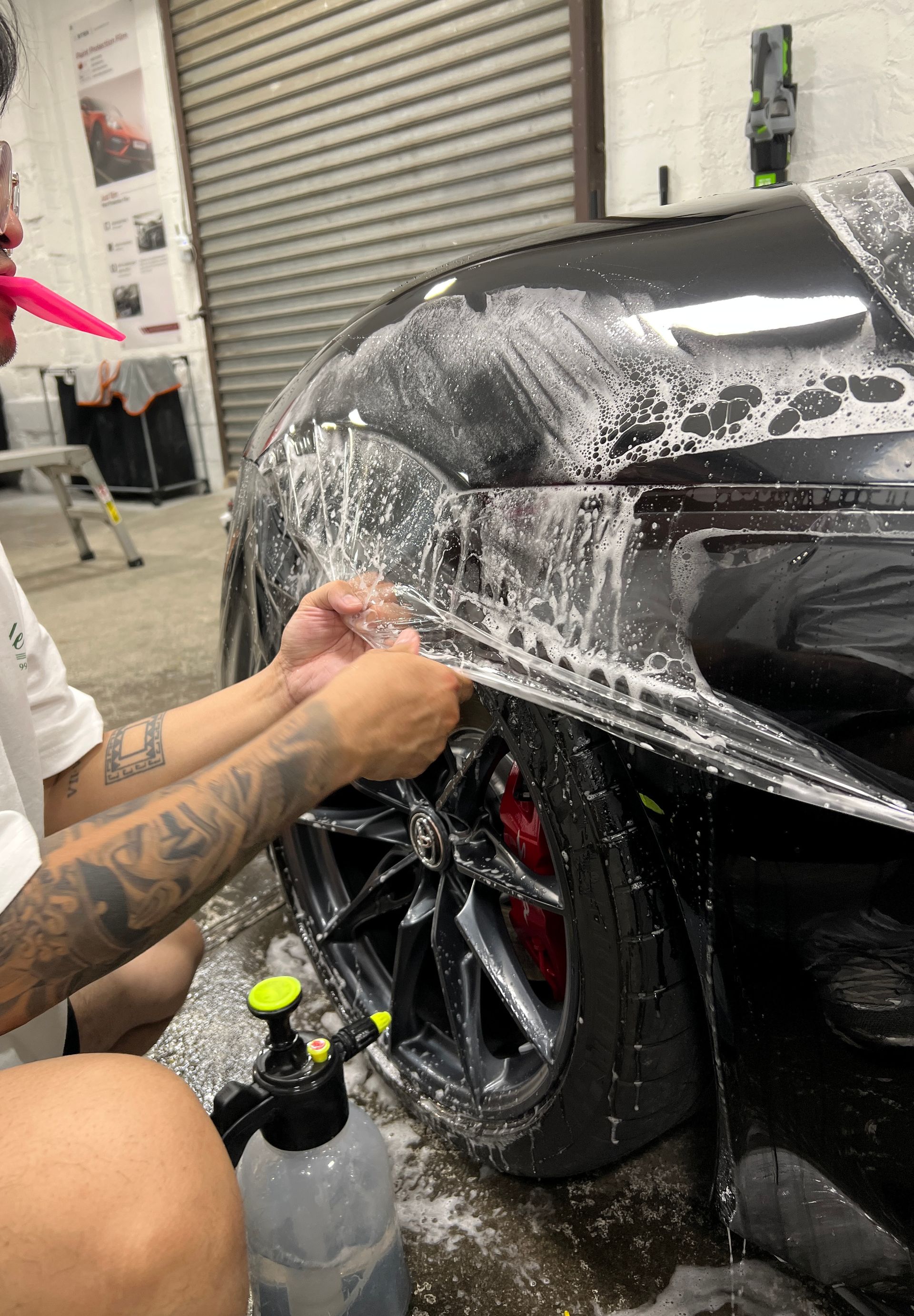 Hand applying protective film to a white car hood with a heat gun nearby