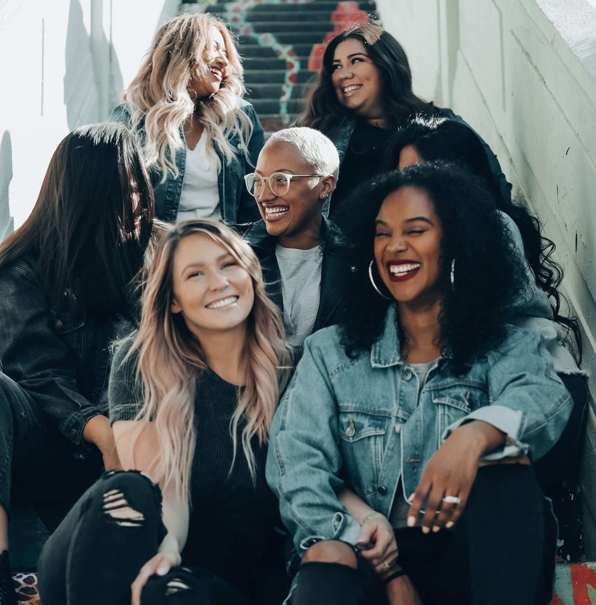 Group of smiling people sitting on outdoor steps, wearing denim and casual clothing.