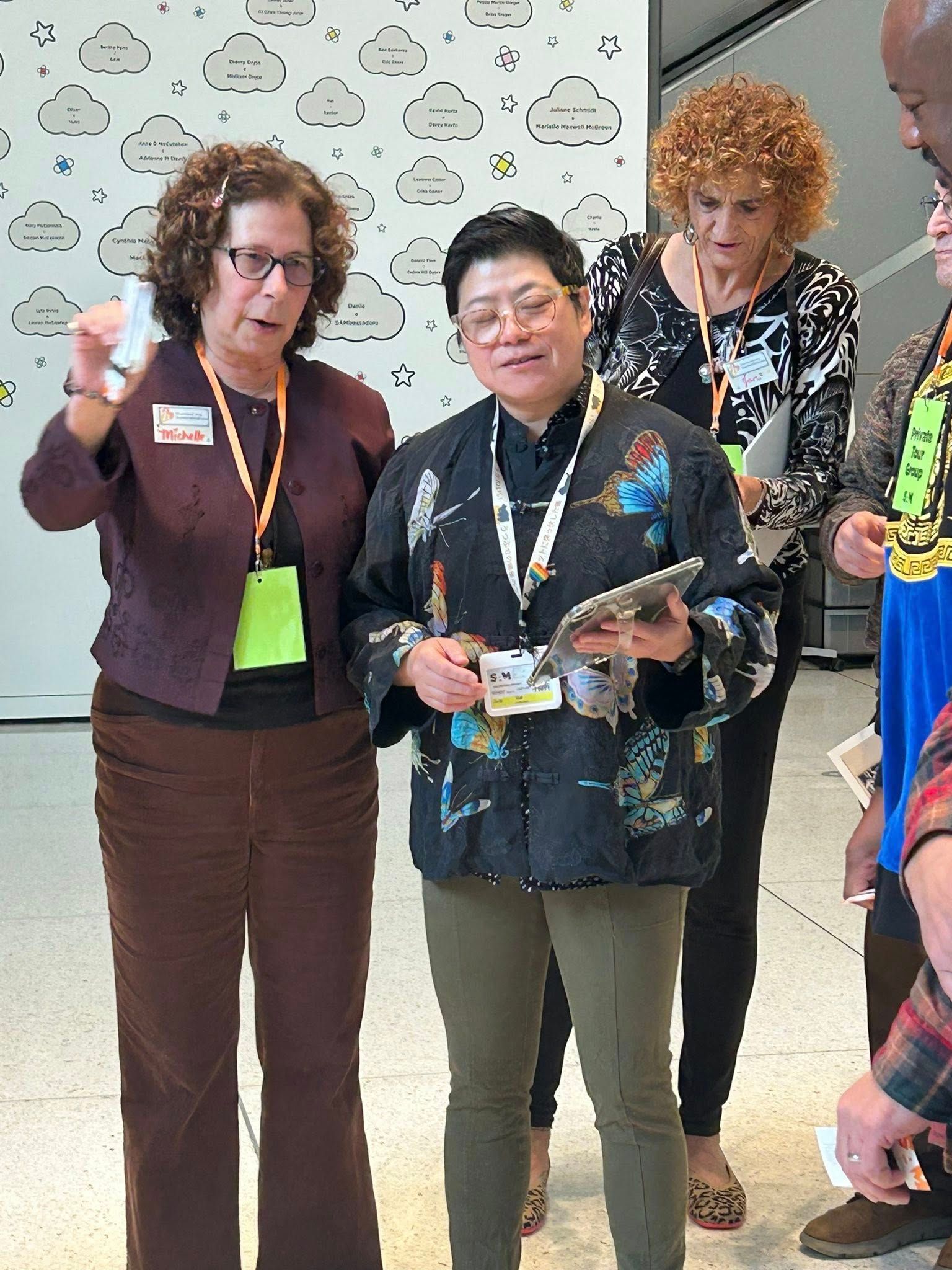 Two women and two people look at a tablet. One woman points, another holds the tablet, and two others observe.