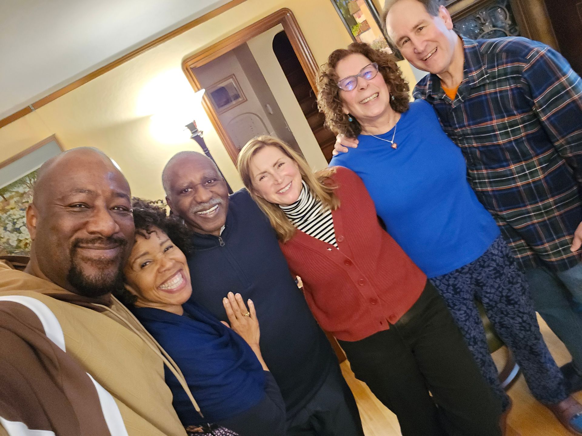 Six people smile, shoulder-to-shoulder, in a warmly lit room.