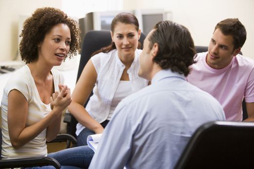 Four people in an office setting engaged in a discussion, two women and two men.