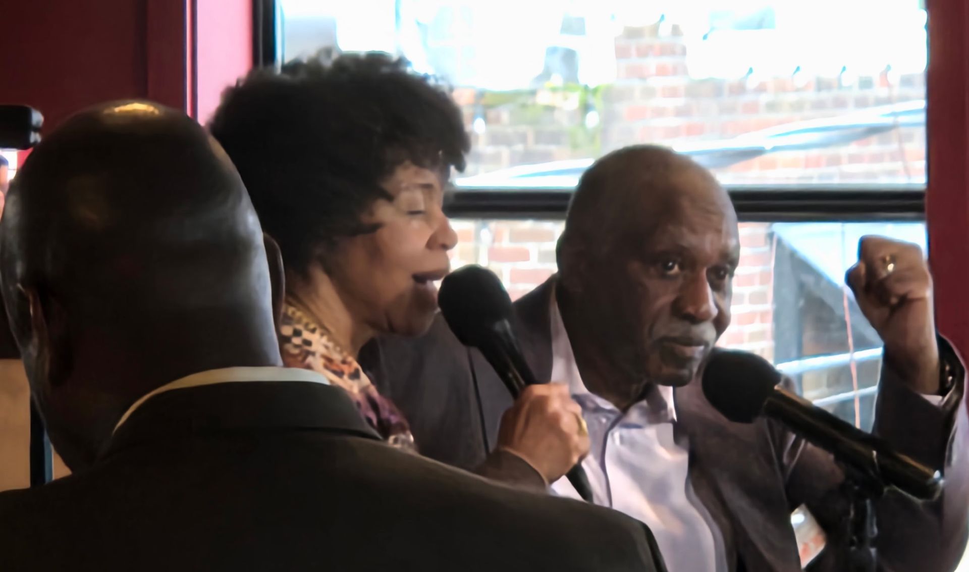 Two people speaking into microphones, one with a raised fist.