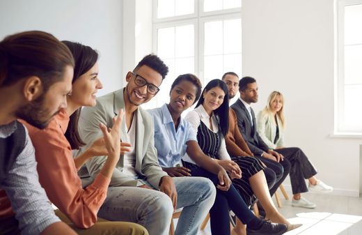 Group of people sitting in a row, talking and smiling in a well-lit room.