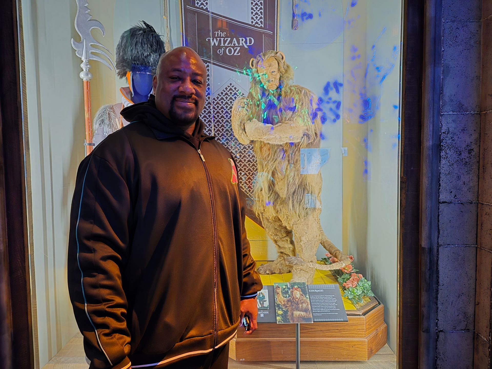 Man posing in front of a Wizard of Oz display. The display features a sculpture and signs.