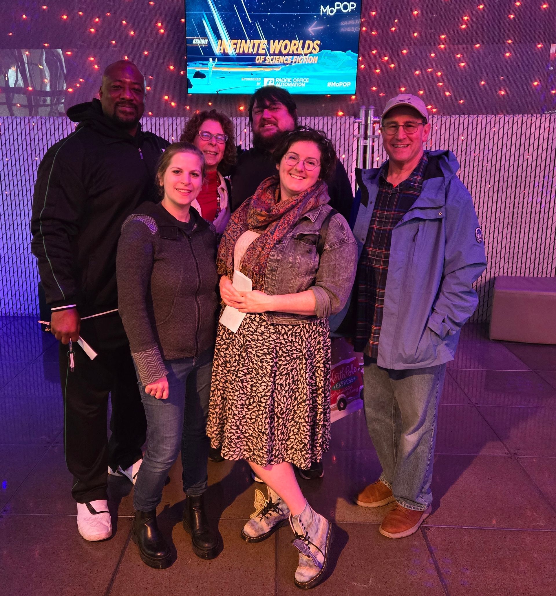 Group of six people posing in front of a colorful backdrop. Two women in the front.