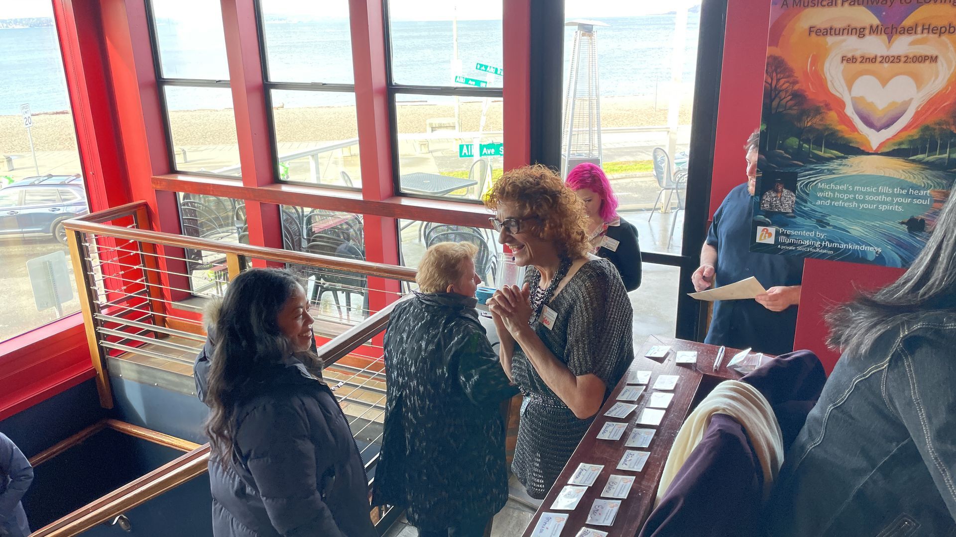 People interacting indoors near a window with a beach view. There's a table with cards and a poster.