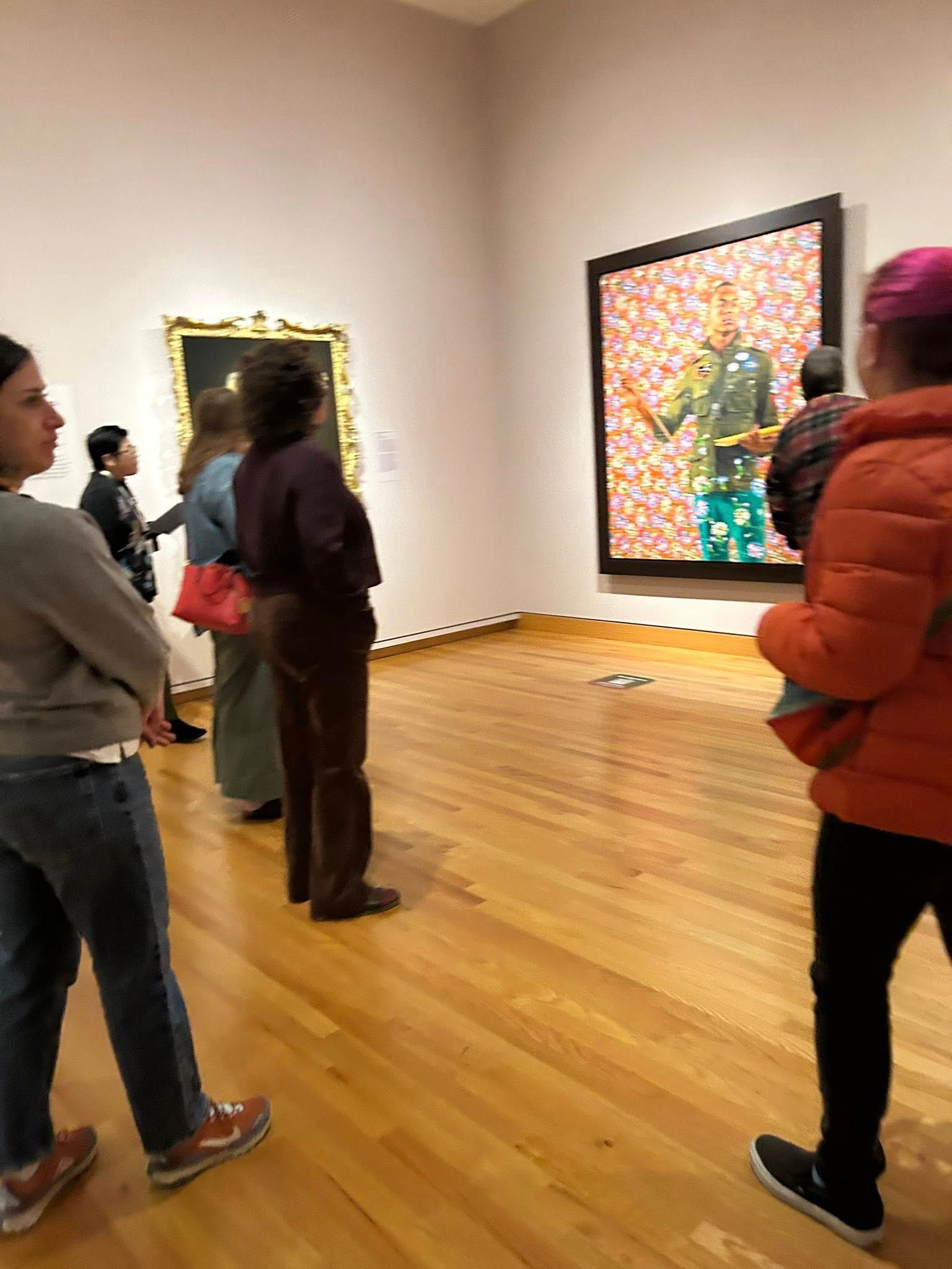 People viewing art in a gallery. One person holds a child. Bright painting on the right.