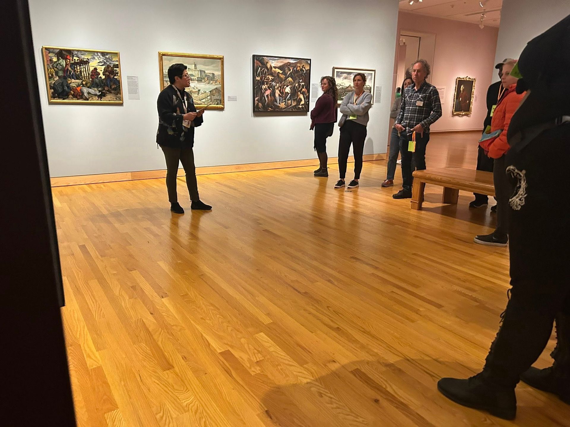 Tour guide speaking to a group in an art gallery, paintings on the wall.