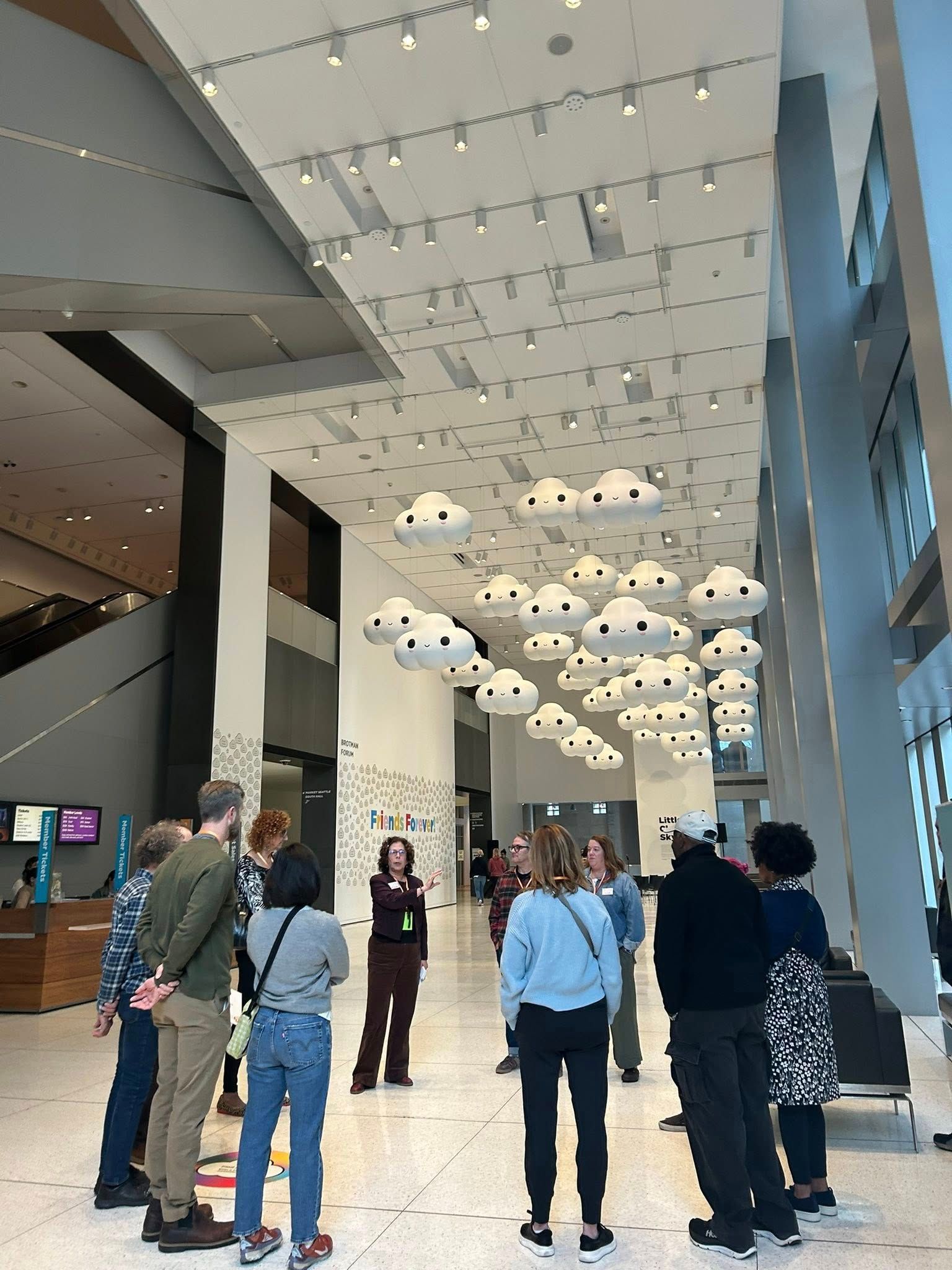 People viewing cloud art installation in a modern building with high ceilings and large windows.