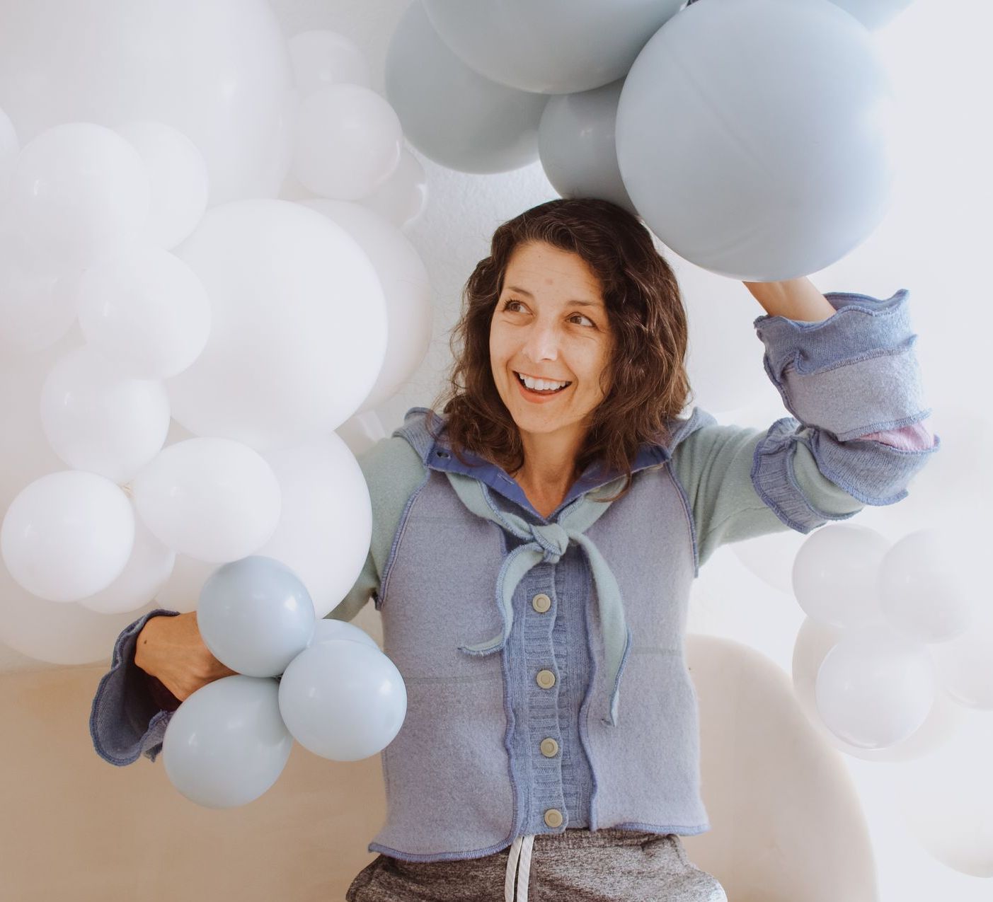 Woman smiling, holding blue balloons with a backdrop of white and blue balloons.