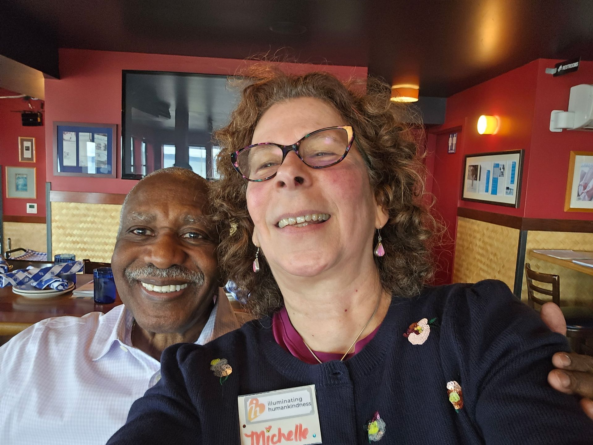 Smiling man and woman pose for selfie inside a restaurant with red walls.