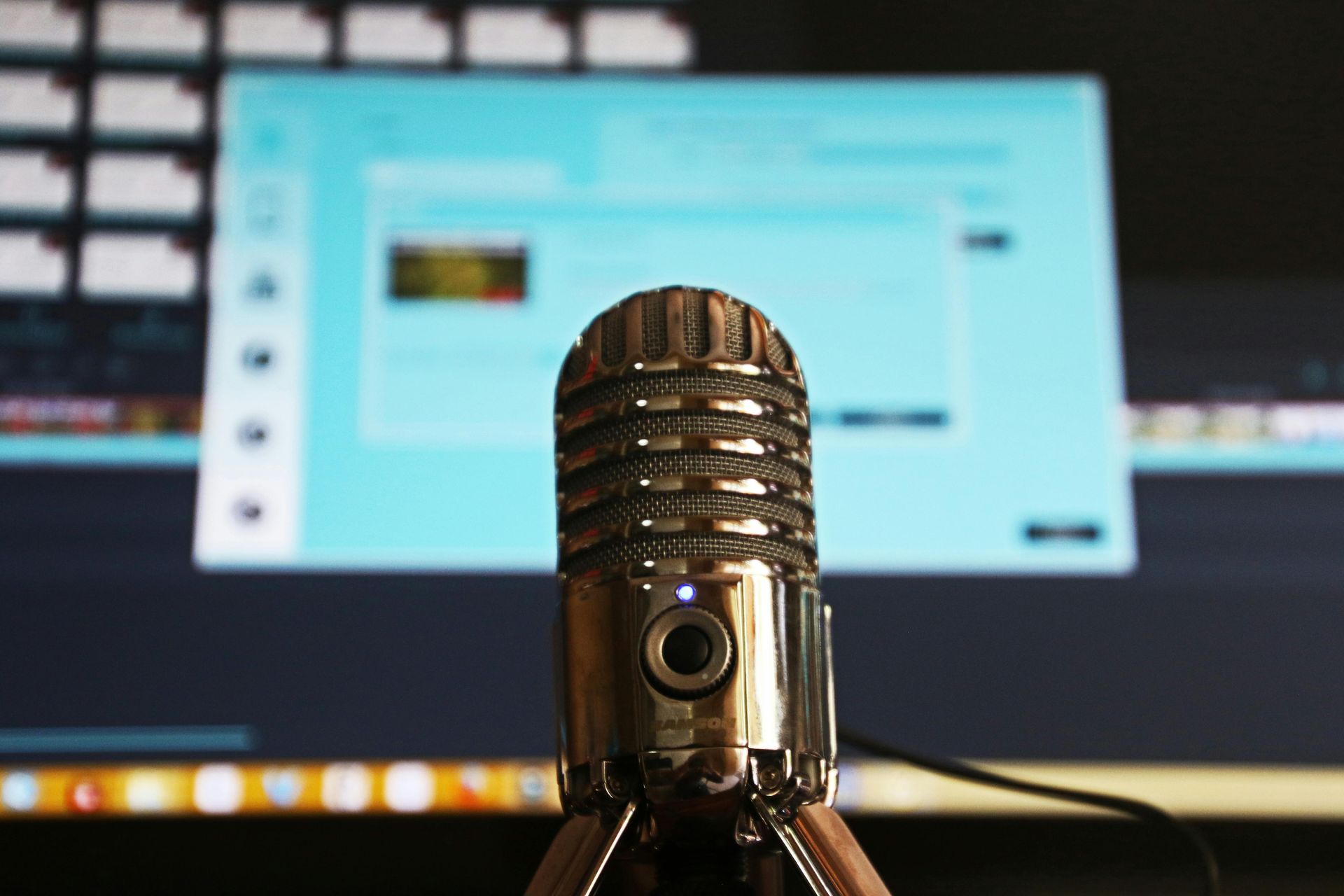 Silver microphone in front of a computer screen, with a blurry interface visible.
