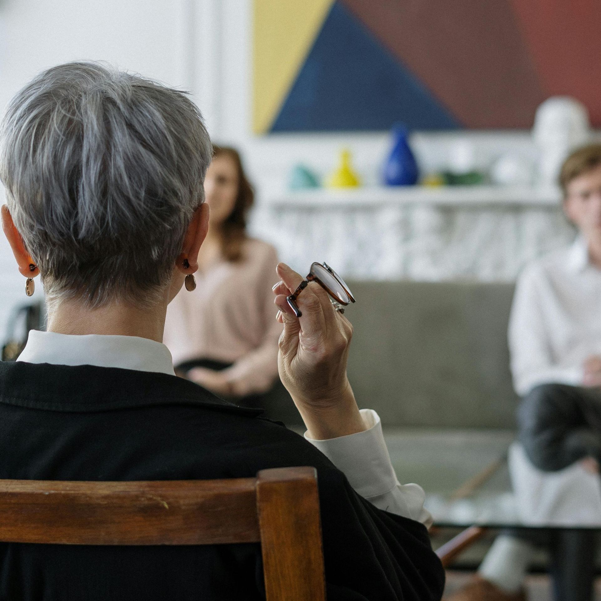 Read Full Letter of Comment Therapist with glasses, facing clients during a session. Other people are seated in the background.