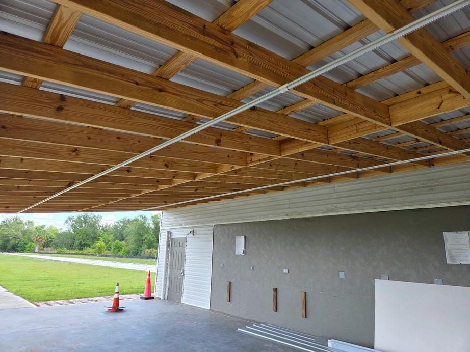 Covered outdoor patio under construction with exposed wooden ceiling and gray wall, two orange cones nearby