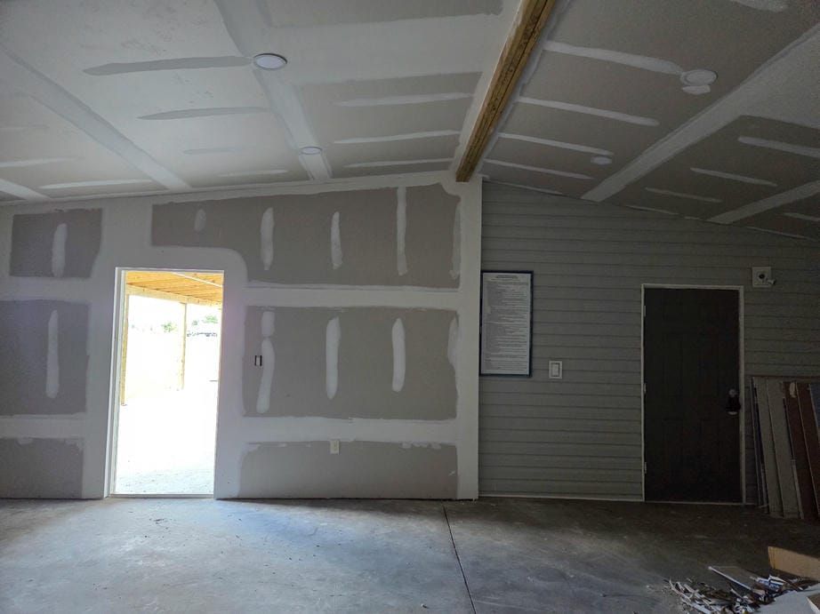 Empty unfinished garage interior with drywall patches, concrete floor, and an open door letting in light