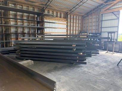 Stacks of dark steel beams stored inside a warehouse workshop.
