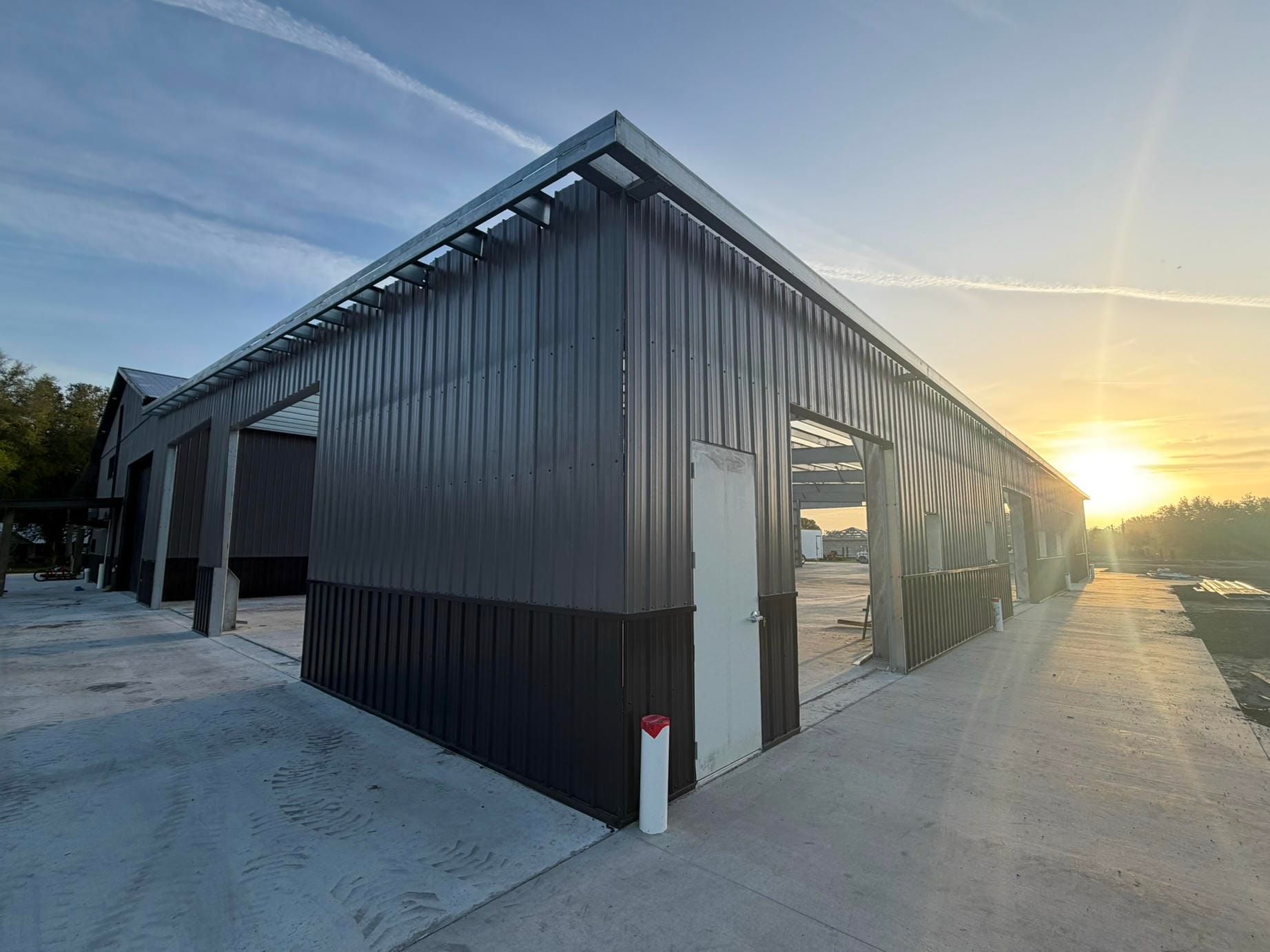 Long, dark metal building with a snow-covered path at sunset