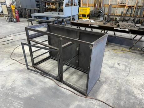 Black welded steel cabinet frame in a workshop, with open shelves and a solid side panel.