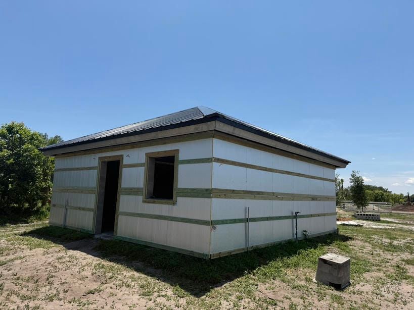 Small white building with green trim and a dark roof on a grassy lot under a clear blue sky
