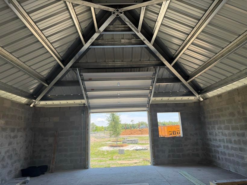 Interior of an unfinished concrete building with a metal roof and open doorway to a grassy field.