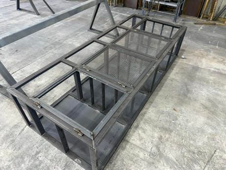 Metal welded frame structure on a concrete floor in a workshop, with mesh panels and open sections
