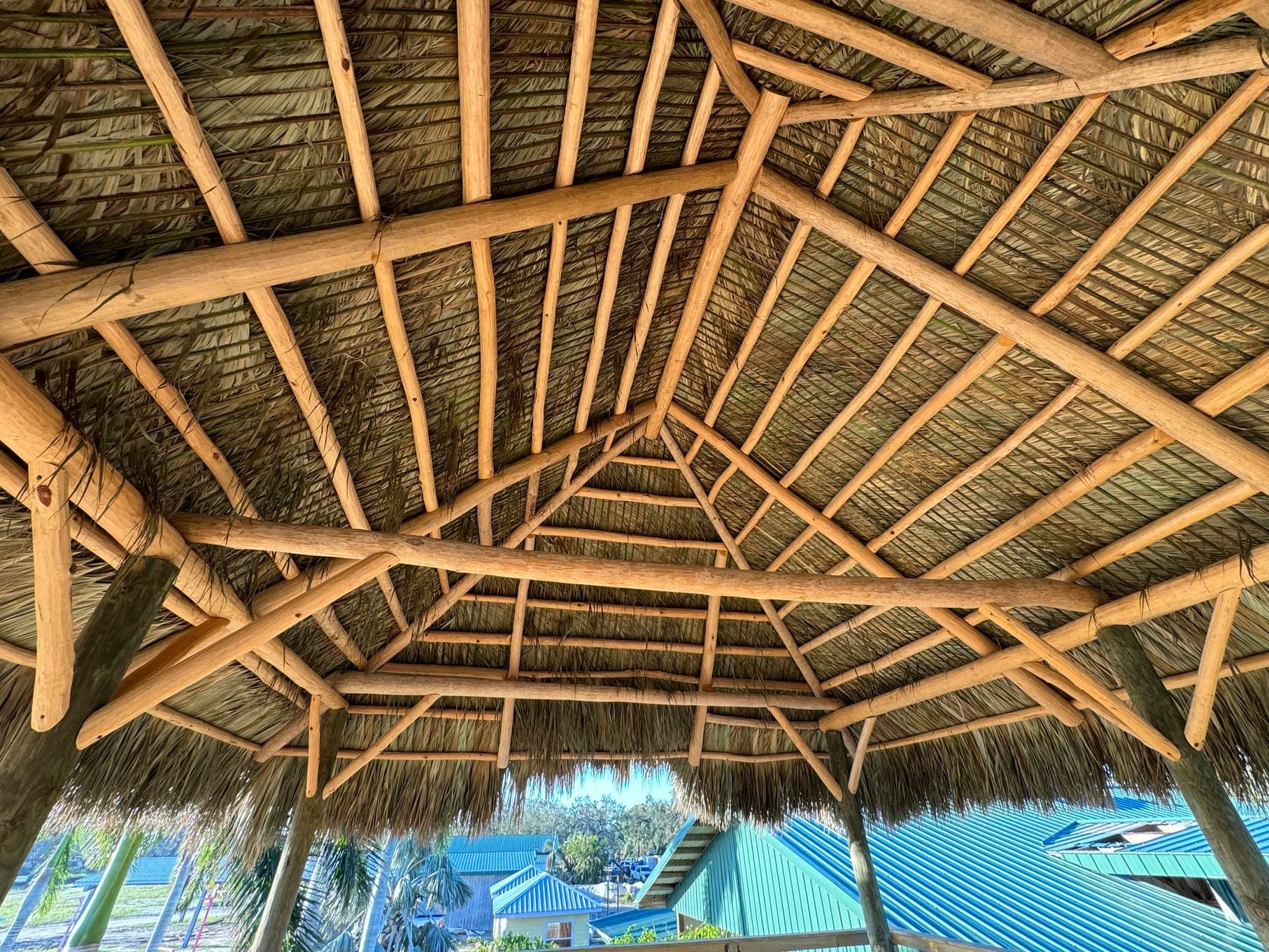Thatched roof interior with wooden beams overlooking a tropical beach and palm trees