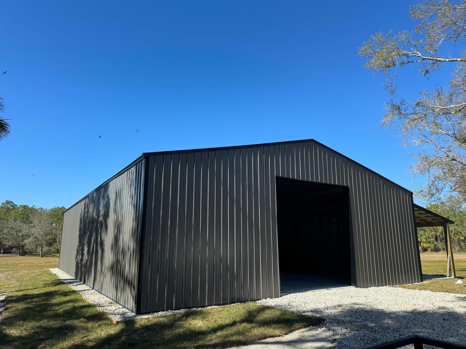 Gray metal barn with a wide open doorway on a gravel driveway under a clear blue sky