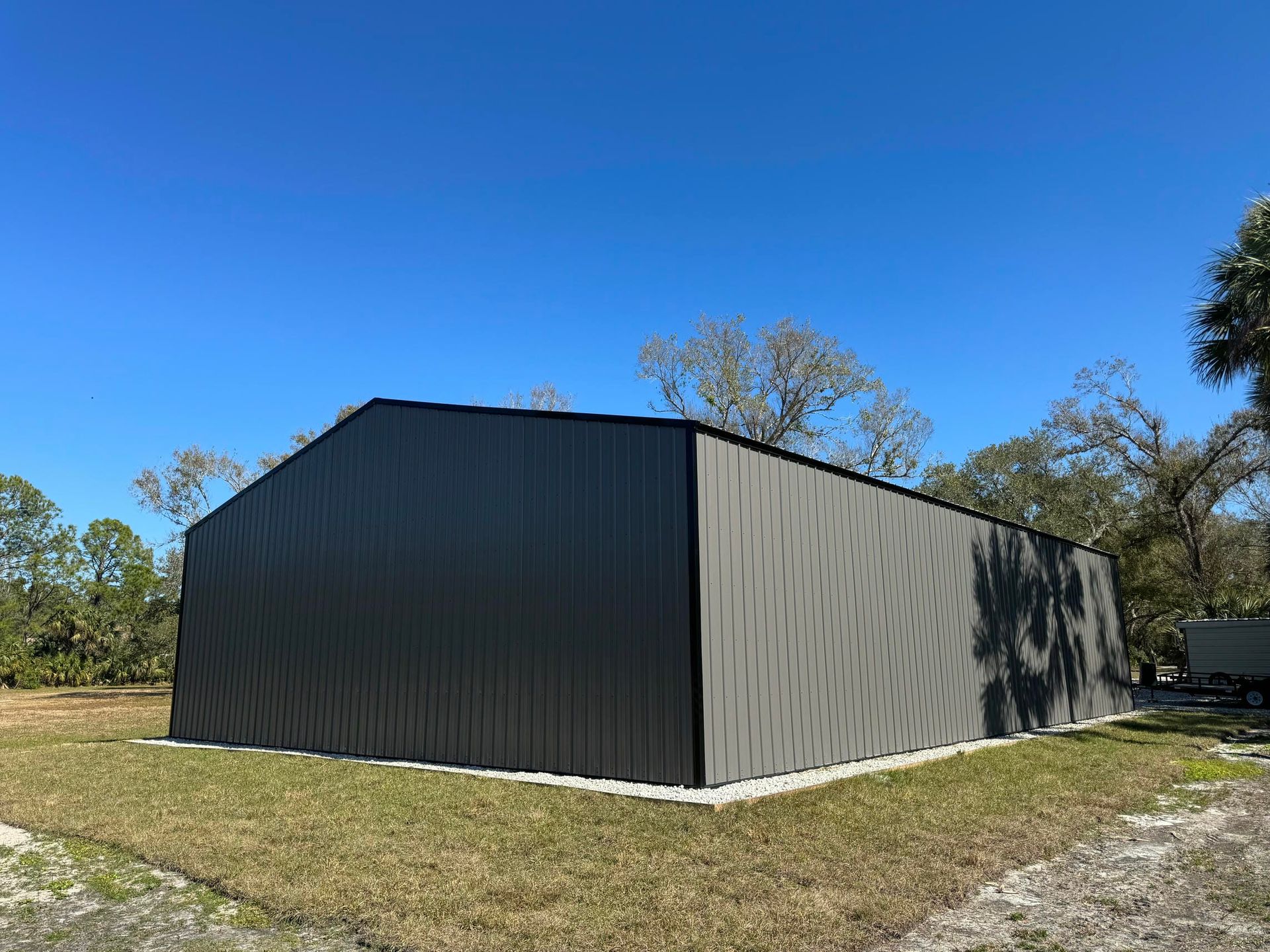 Black metal barn-like building on a grassy lot under a clear blue sky