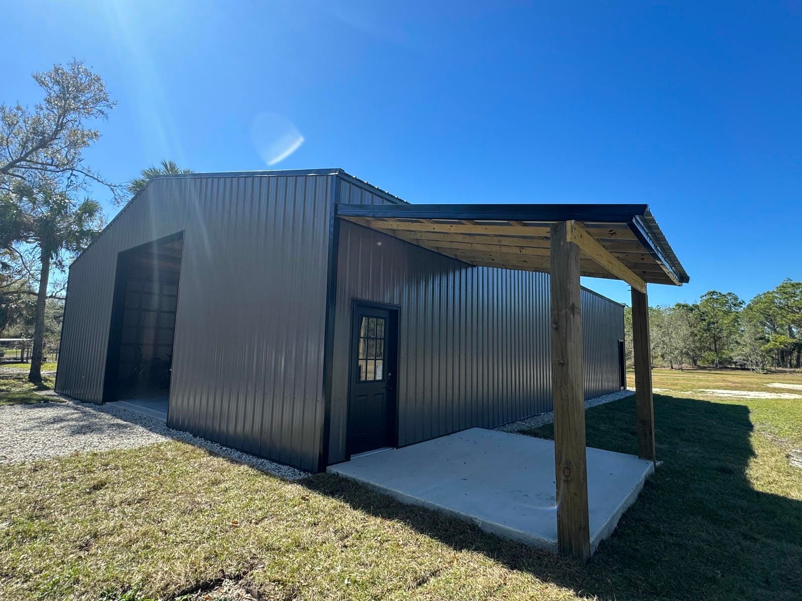 Small corrugated metal shed with a covered porch in a grassy yard under a bright blue sky