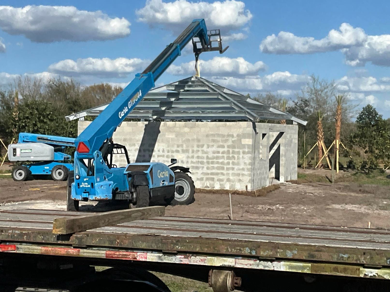 Blue boom lift beside a cinder block building under construction on a cloudy day