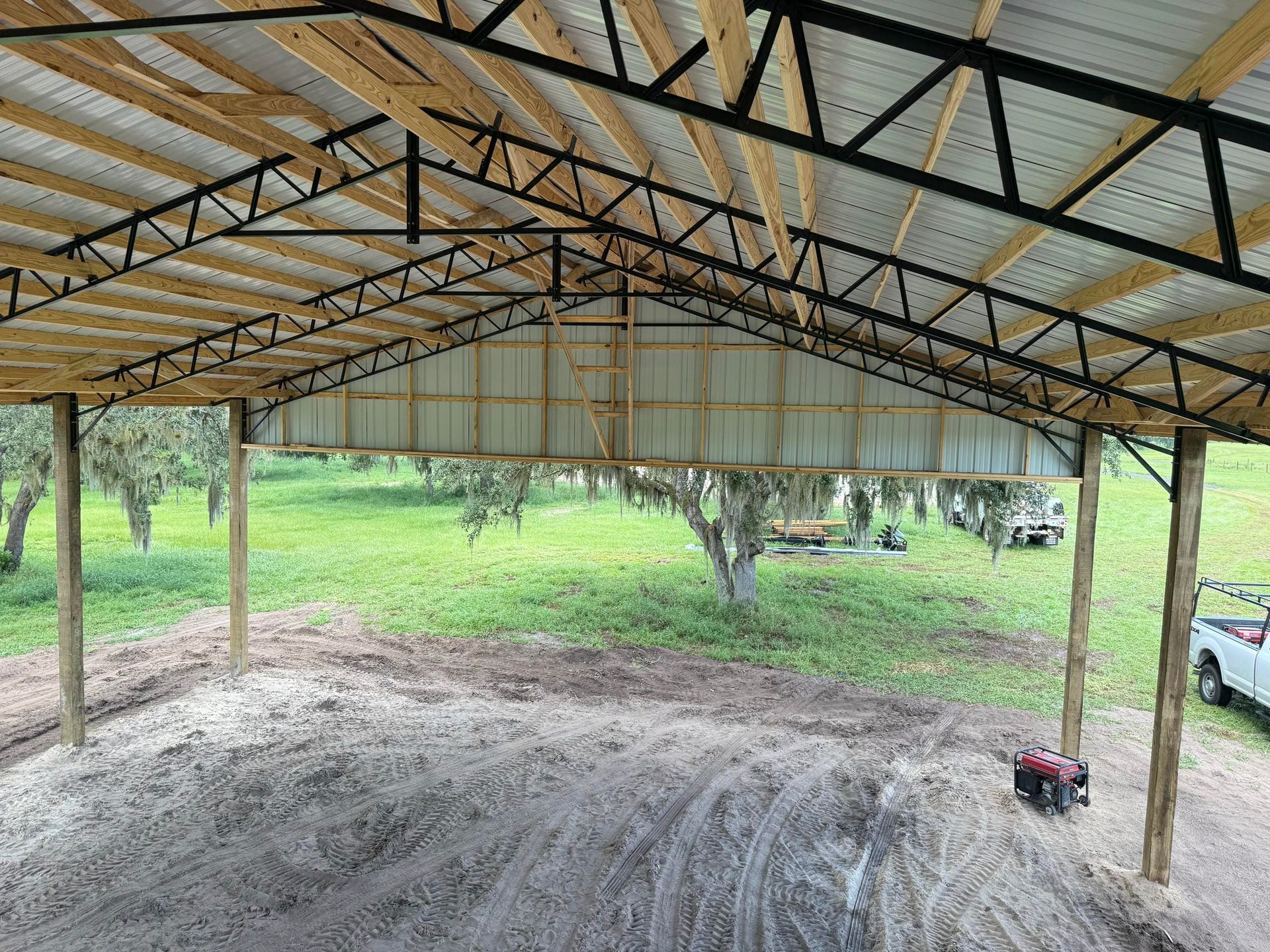 Open-sided shed with metal roof over a dirt floor, looking out onto a green grassy yard.