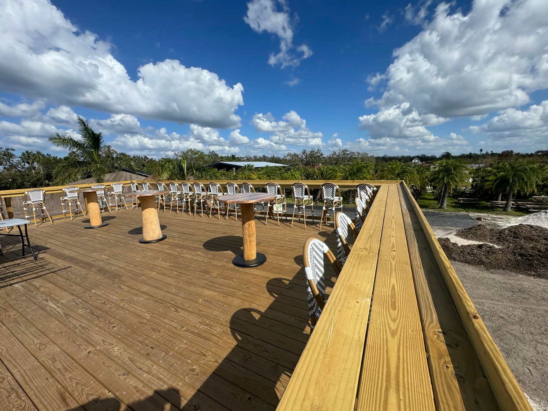 Wooden boardwalk with white chairs and tables under a bright blue sky with clouds