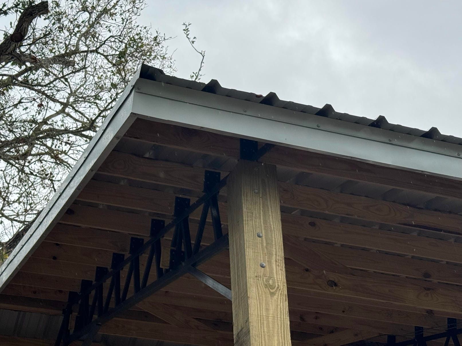Wooden porch roof underside with exposed beams and a central support post against cloudy sky
