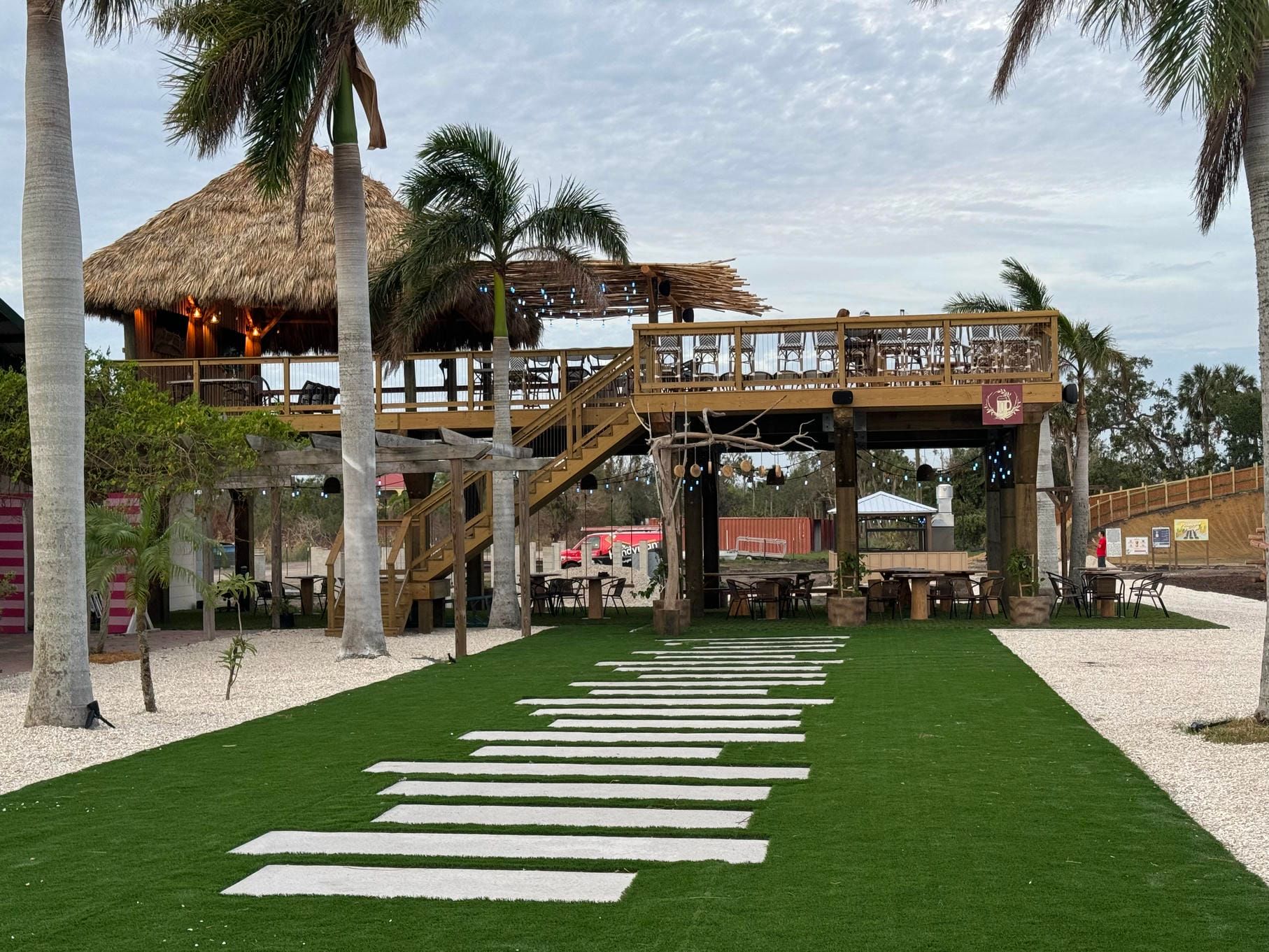 Tropical resort walkway with stepping stones, palm trees, and a thatched-roof deck over a white sand path