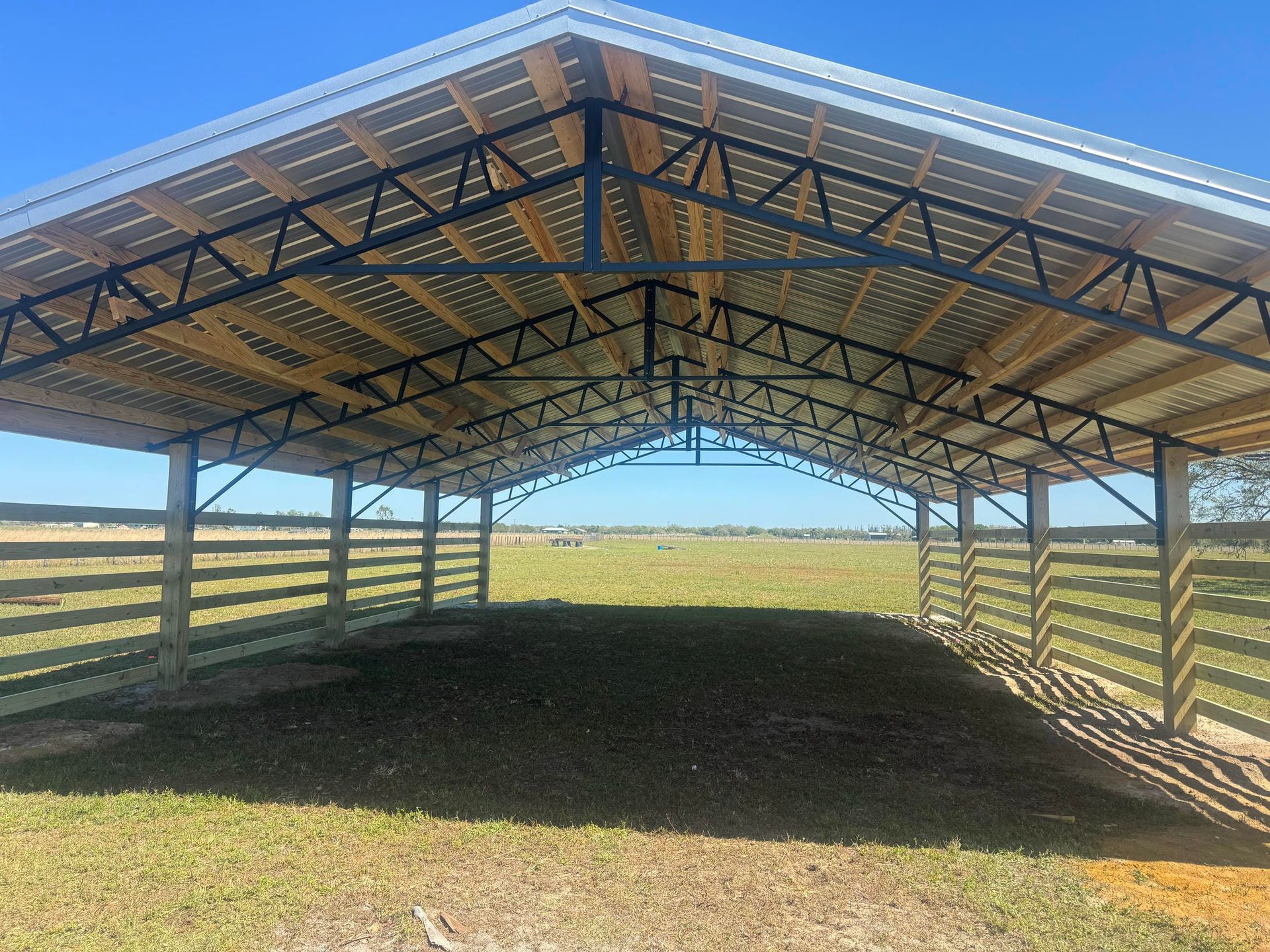 Open-sided metal livestock shelter with corrugated roof in a grassy field