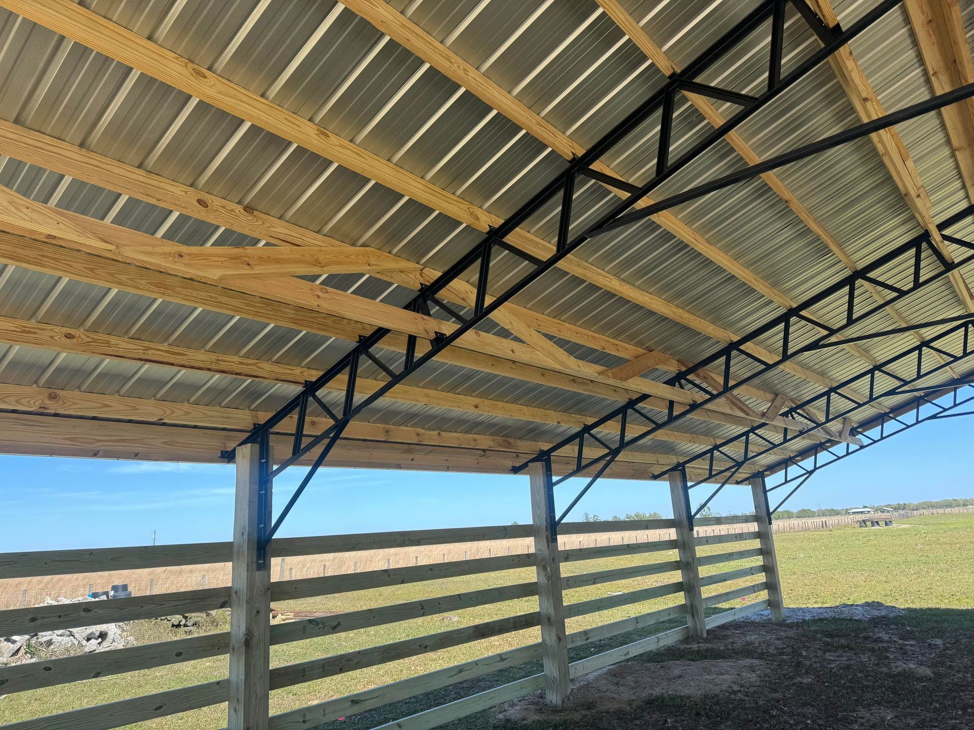 Covered farm shelter with corrugated roof and metal trusses overlooking a grassy field