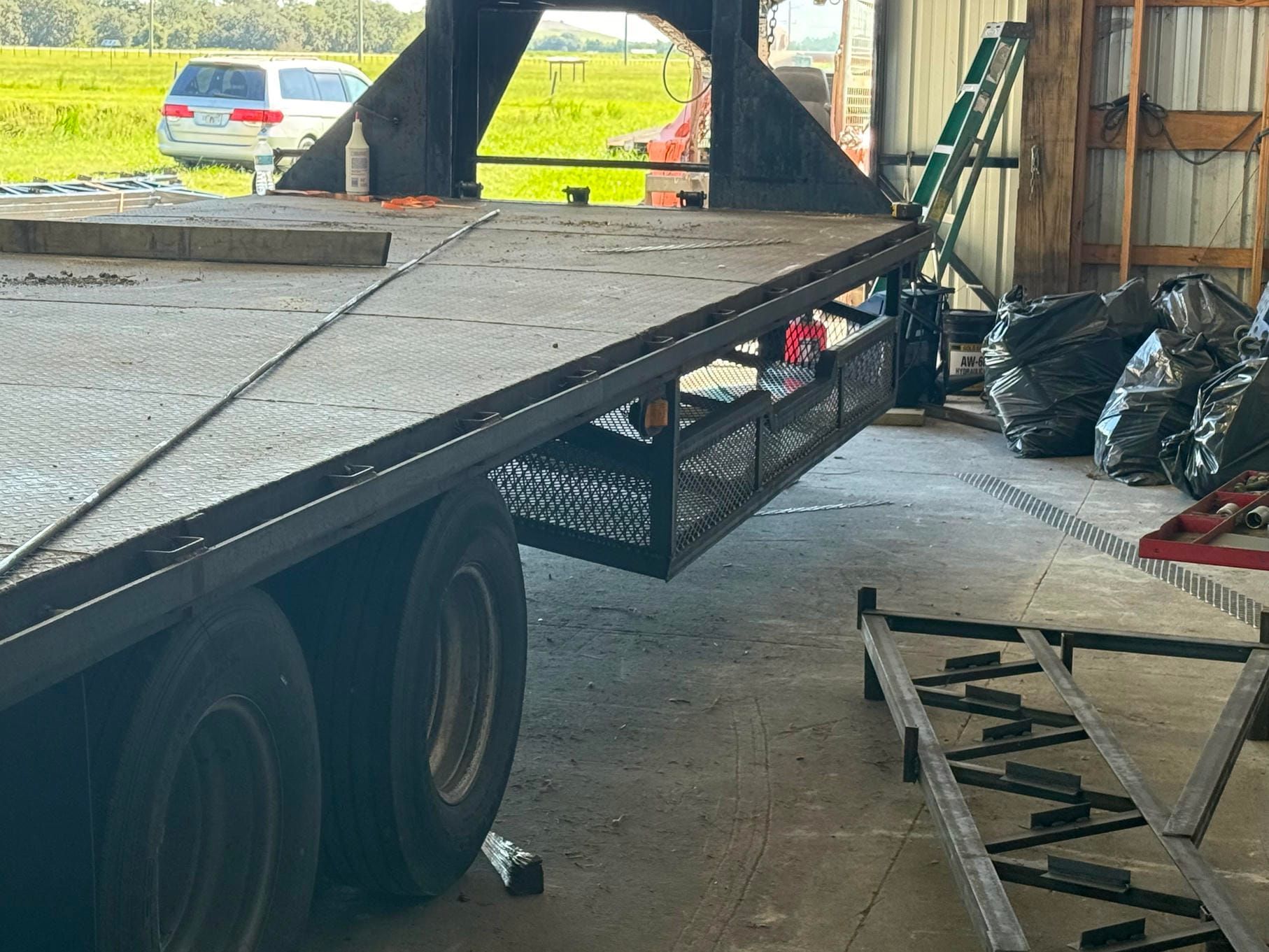 Flatbed trailer with a raised ramp inside a barn, with two stacked black tires underneath.