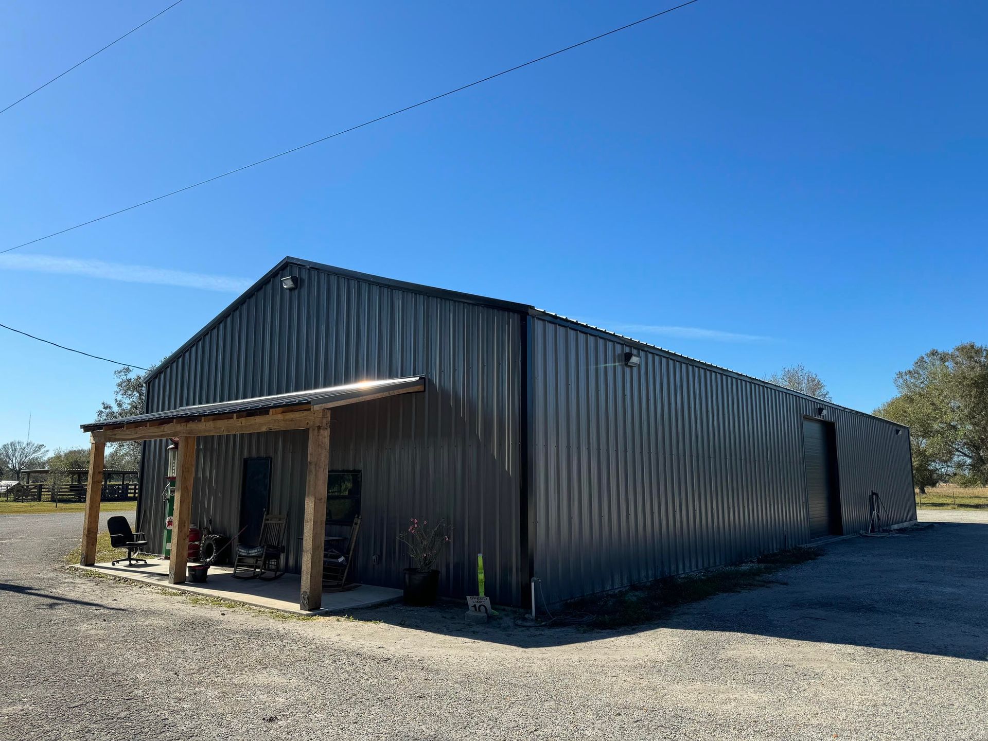 Large corrugated metal warehouse with a small porch, set on a gravel lot under a clear blue sky