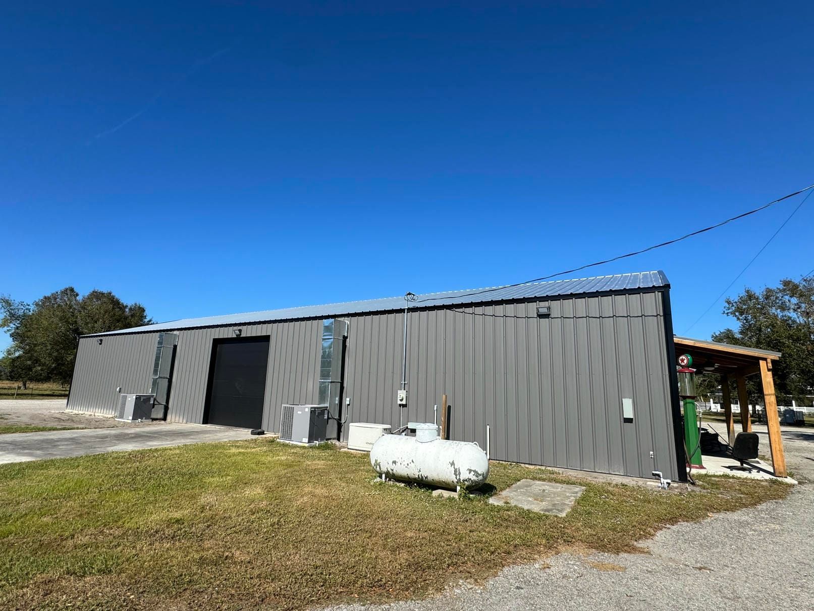 Gray metal building with a black door, white tank outside, and clear blue sky over a grassy lot