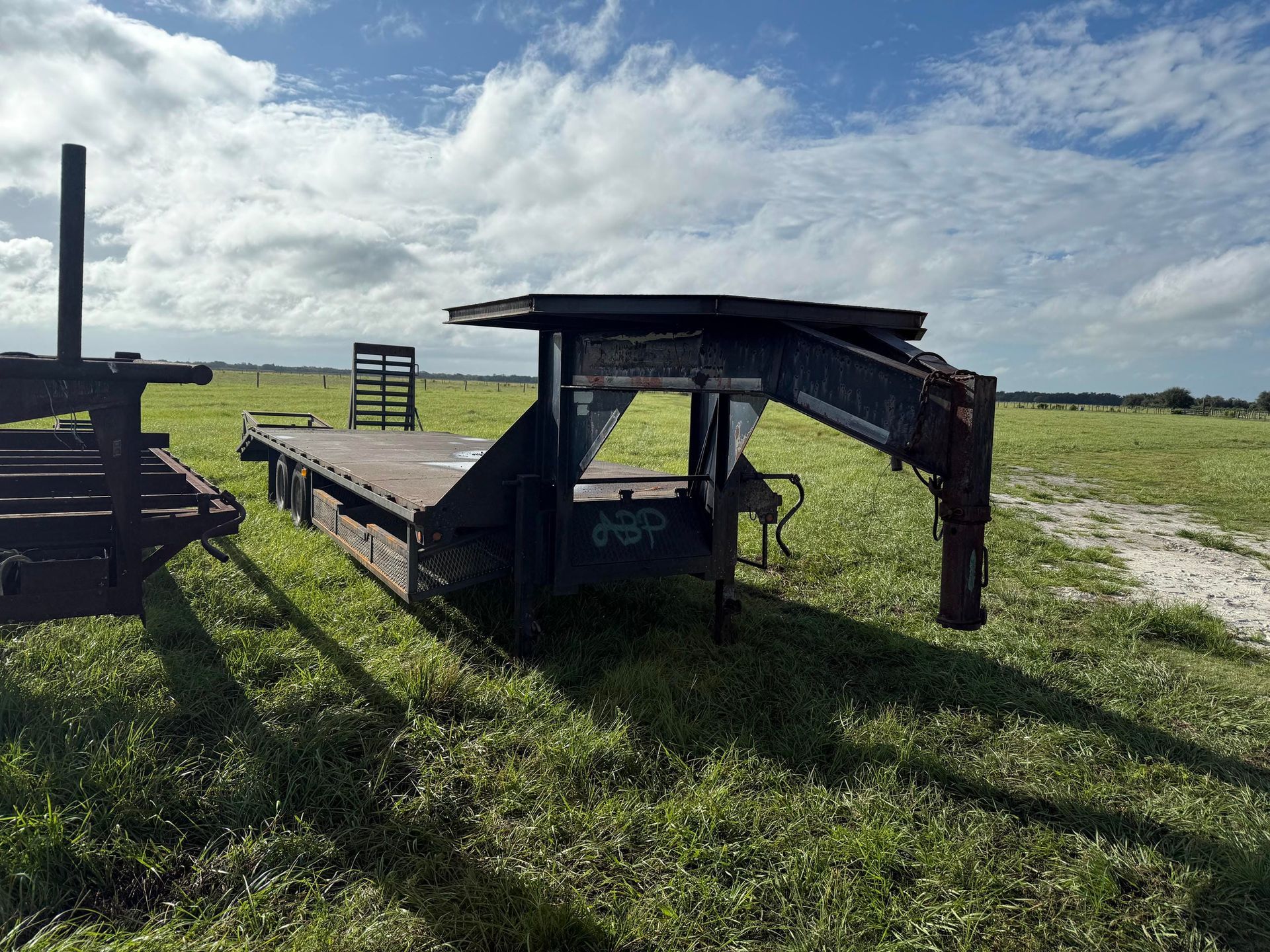 Damaged black trailer in a grassy field under a cloudy sky, with a bent roof and open sides