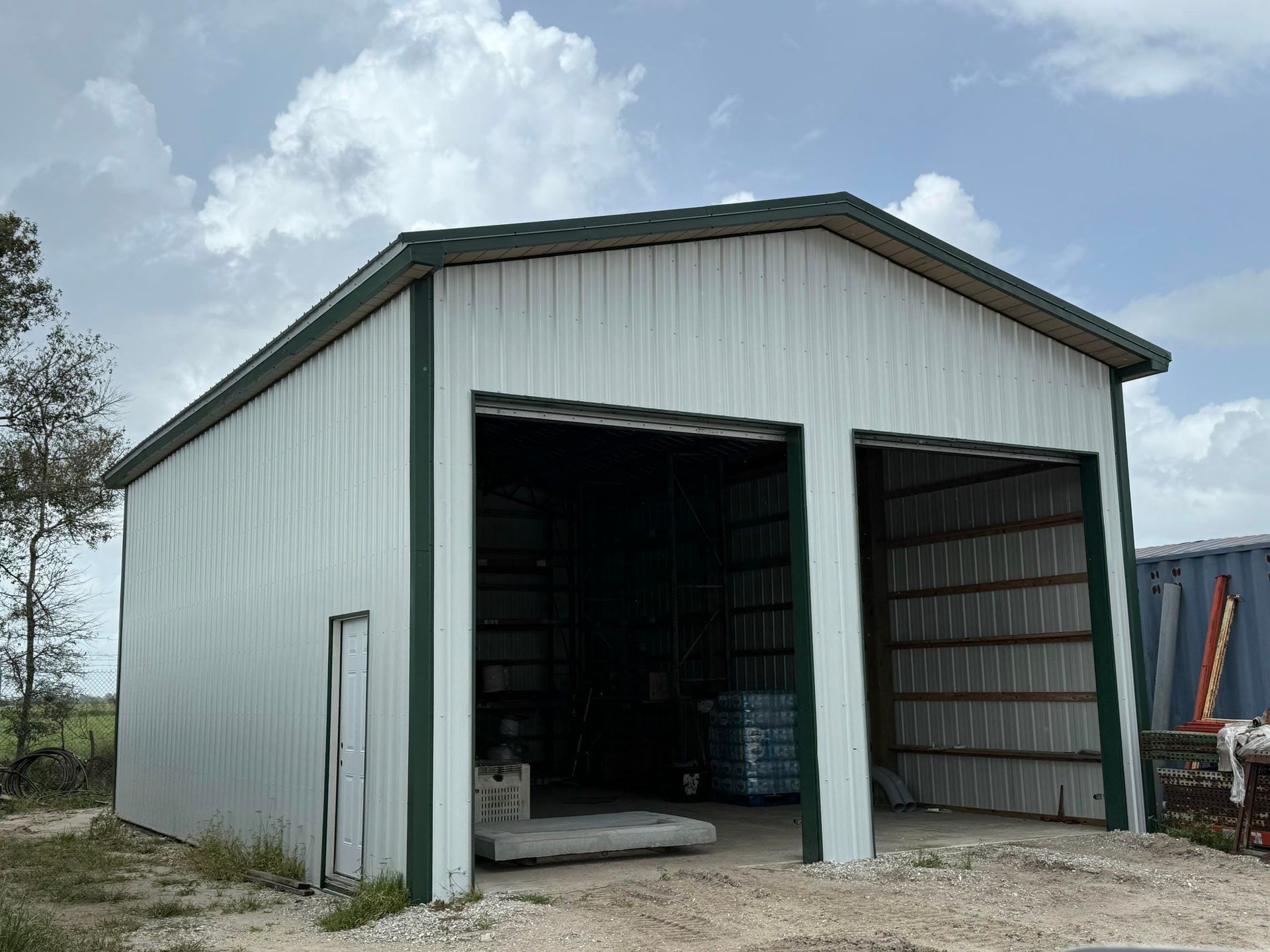 White metal barn with open front doors on a grassy lot under a cloudy sky