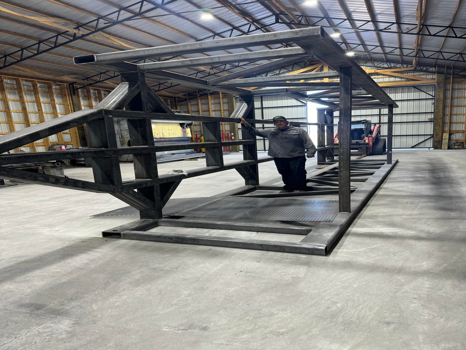 Large black metal truss structure on a warehouse floor, with workers in the background.